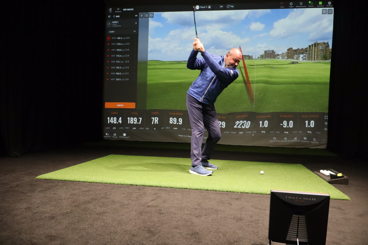 Golfer mid-backswing with shot data displayed on TrackMan screen