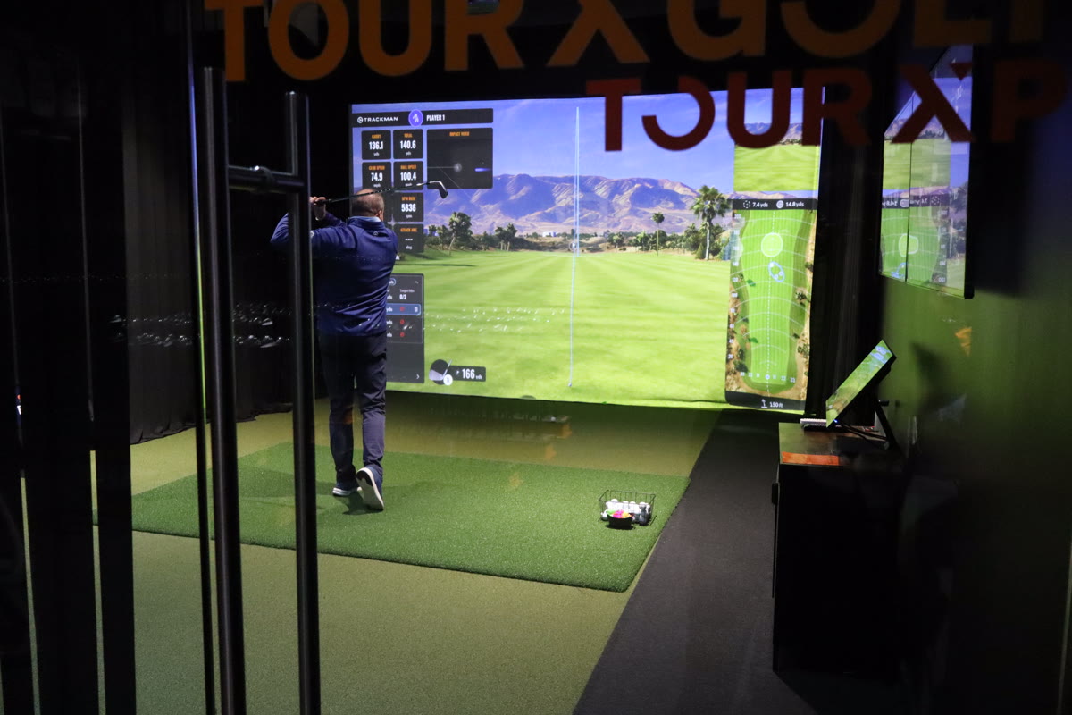 View through glass showing TOUR X GOLF branding and simulator bay